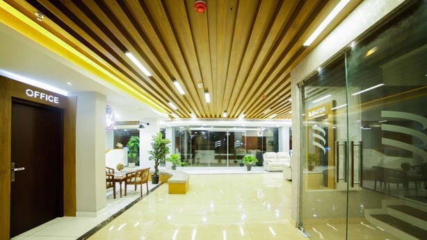 Un moderno vestíbulo de oficina con techo de madera, un mostrador de recepción y una zona de estar con plantas.