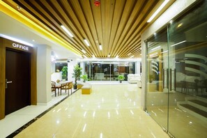Un moderno vestíbulo de oficina con techo de madera, un mostrador de recepción y una zona de estar con plantas.