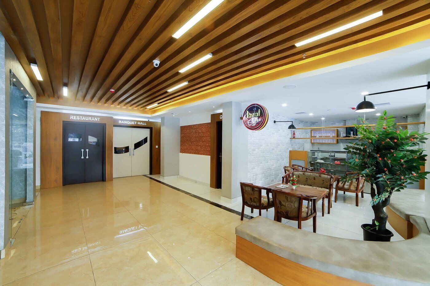 Un vestíbulo moderno con techo de madera, mostrador de recepción, zona de estar con sillas y una mesa, y un letrero para un restaurante y salón de banquetes.