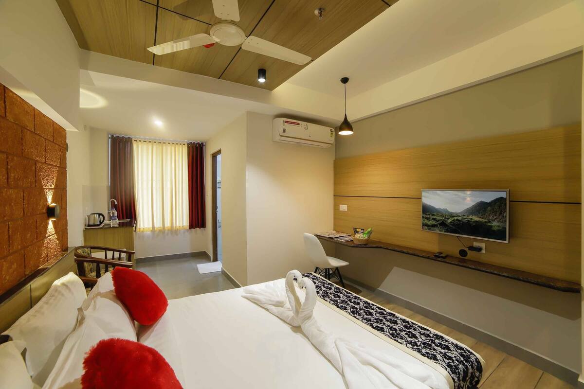 Quarto de hotel com cama, televisão fixada na parede, ventilador de teto e ar condicionado.