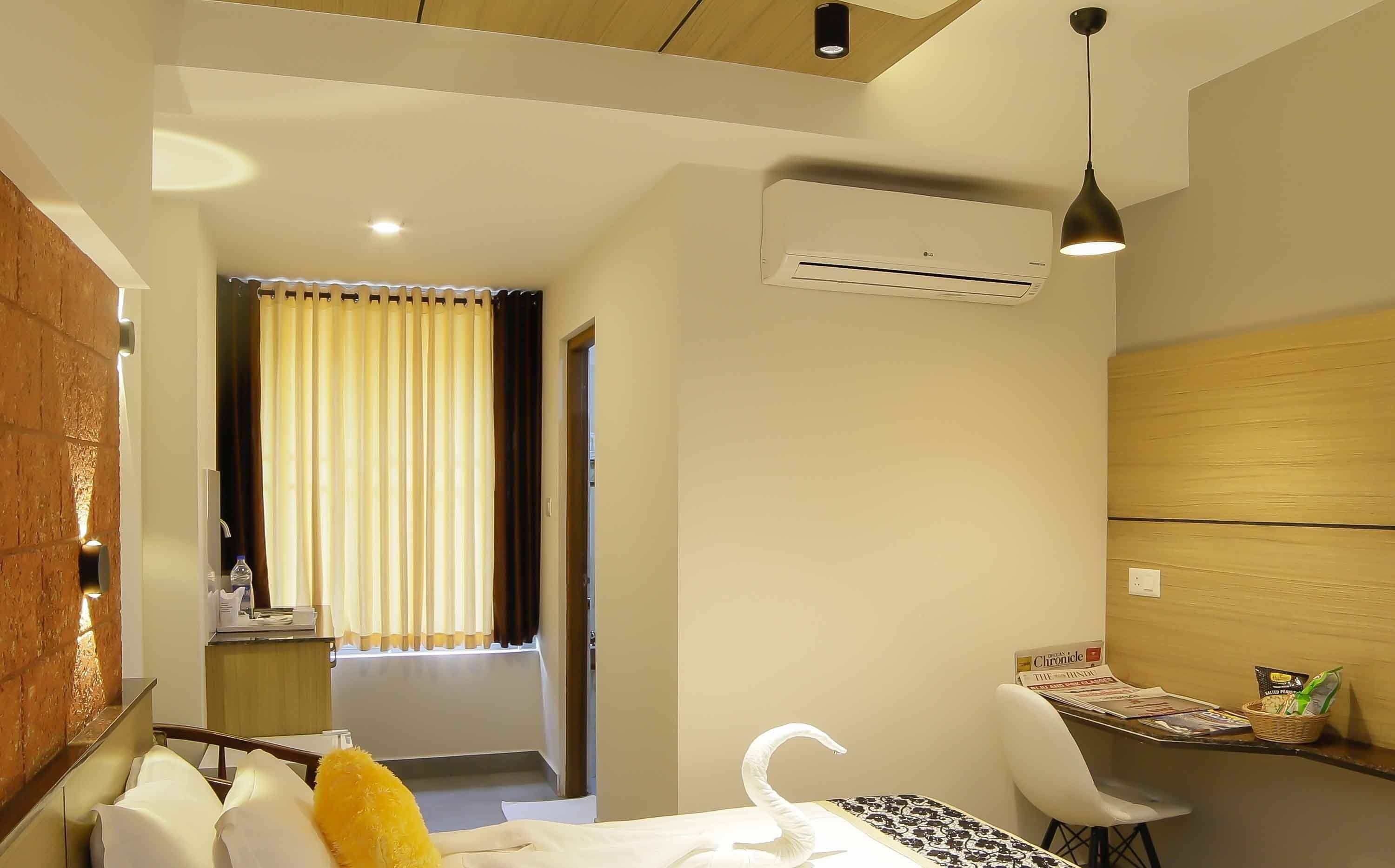 Habitación de hotel con cama, una mesita con silla, aire acondicionado en la pared y ventana con cortinas.