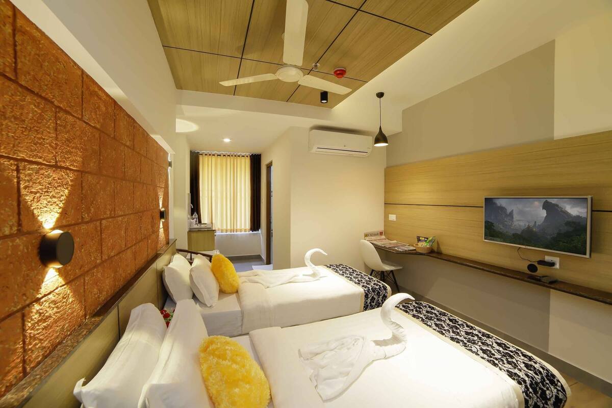Quarto de hotel com duas camas, uma televisão, um ventilador de teto e uma parede de destaque em madeira.