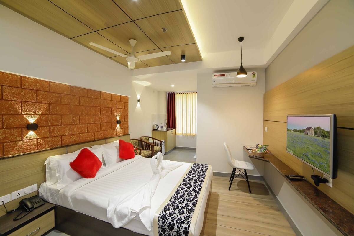 Quarto de hotel com cama, escrivaninha, cadeira, televisão e ar condicionado fixado na parede.
