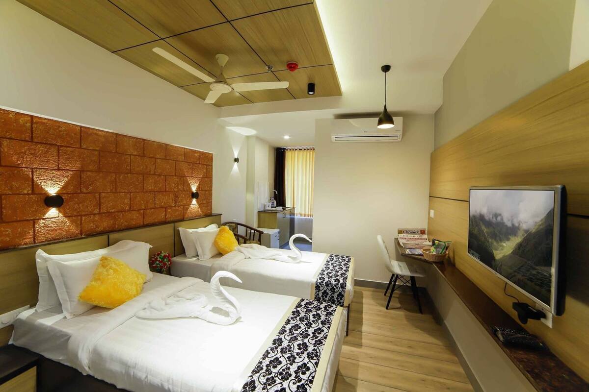 Quarto de hotel com duas camas, televisão, escrivaninha e banheiro visível por uma porta aberta.
