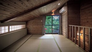 Habitación con suelo de tatami, paredes de madera, techo inclinado y un ventanal con vistas a la vegetación.