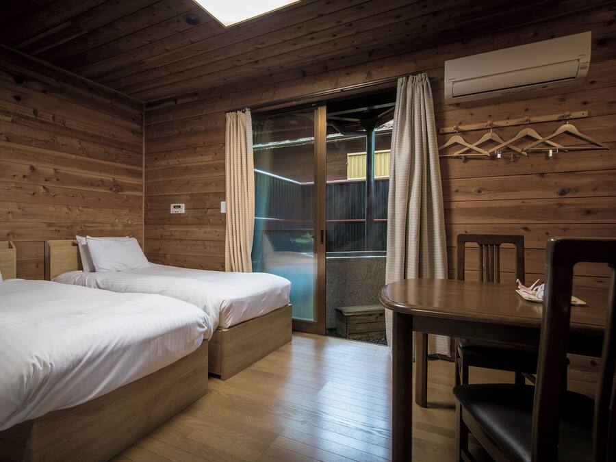 A wooden cabin room with two beds, a dining table, and an air conditioning unit.