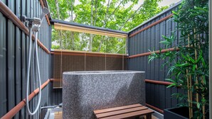 Un jacuzzi con banco de madera, rodeado de plantas de bambú y una ventana con persianas.