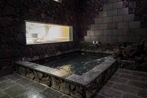 A stone-walled hot tub with a window, stone steps, and a stone wall. - FUJIYAMA INN CONIFER (Fujiyoshida)