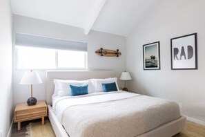 Une chambre à coucher avec un lit, deux tables de chevet, une fenêtre et des œuvres d’art murales.