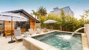 En pool med solstolar och parasoller, omgiven av grönska och modern arkitektur.