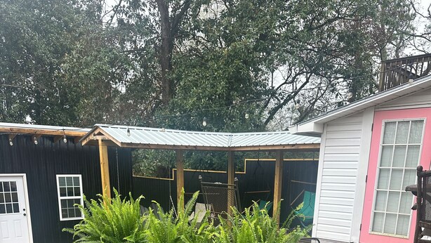 A covered outdoor area with a wooden deck, a black shed, and a pink building. - Downtown Carrollton - Backyard Bungalow (Carrollton)