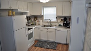 A compact kitchen with white cabinets, a refrigerator, stove, sink, and a microwave. - Downtown Carrollton - Backyard Bungalow (Carrollton)
