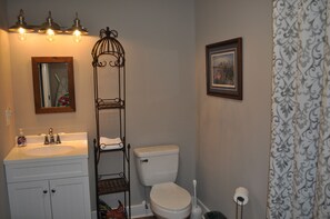 Ein Badezimmer mit einem weißen Waschbecken, einer Toilette, einem Metallregal und einem gerahmten Bild an der Wand.