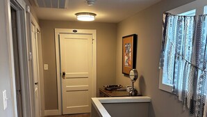 A hallway with carpeted flooring, a white door, a framed picture on the wall, and a window with patterned curtains. - Downtown Carrollton - Backyard Bungalow (Carrollton)