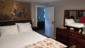 A hotel room with a bed, a dresser, a mirror, a painting, and a desk with a lamp. - Downtown Carrollton - Backyard Bungalow (Carrollton)