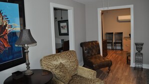 A living room with a sofa, a leather armchair, a floor lamp, and a painting on the wall. - Downtown Carrollton - Backyard Bungalow (Carrollton)