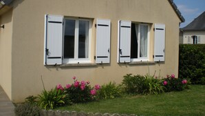 A house with two windows and a garden with pink flowers. - Gite Grandcamp Maisy. (Grandcamp-Maisy)