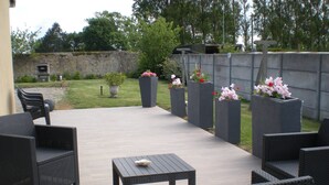 An outdoor patio with wicker furniture, a table, and flower planters. - Gite Grandcamp Maisy. (Grandcamp-Maisy)