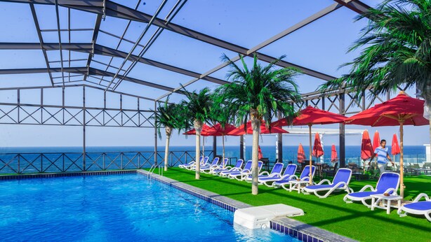 A pool area with blue water, white lounge chairs, red umbrellas, and palm trees. - Porto Said Hotel & Spa (Al-Manasrah)