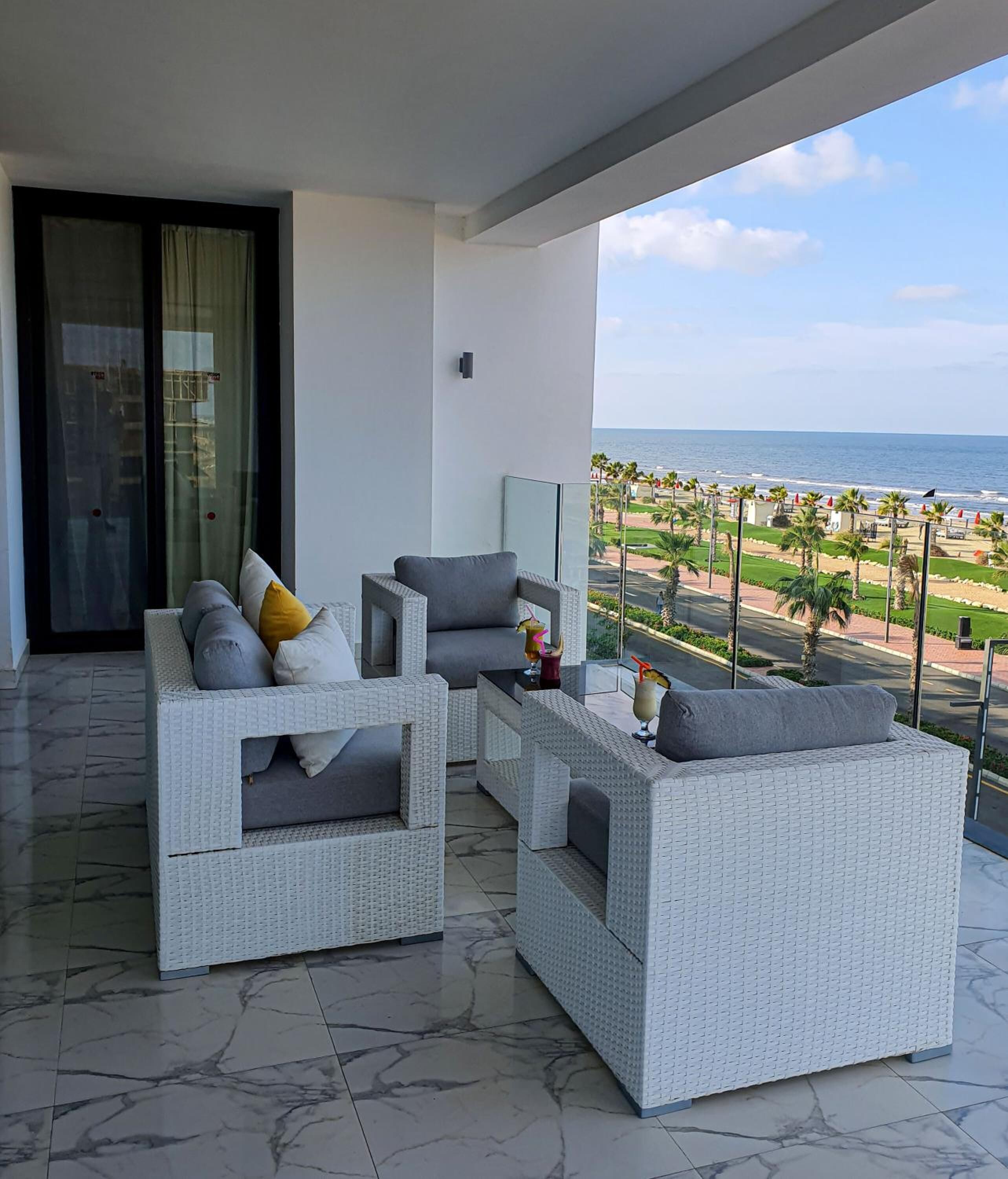 Un balcón con mobiliario de mimbre, una puerta de cristal y vista a la playa y al océano.