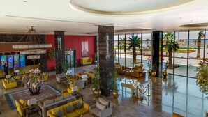 A spacious lobby with yellow and grey seating, large windows, and a central pillar. - Porto Said Hotel & Spa (Al-Manasrah)