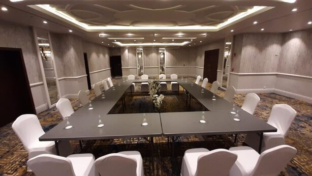 Un salón de conferencias con una larga mesa, sillas blancas y piso alfombrado.
