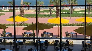 An outdoor seating area with tables and chairs, yellow umbrellas, and a view of the beach and ocean. - Porto Said Hotel & Spa (Al-Manasrah)