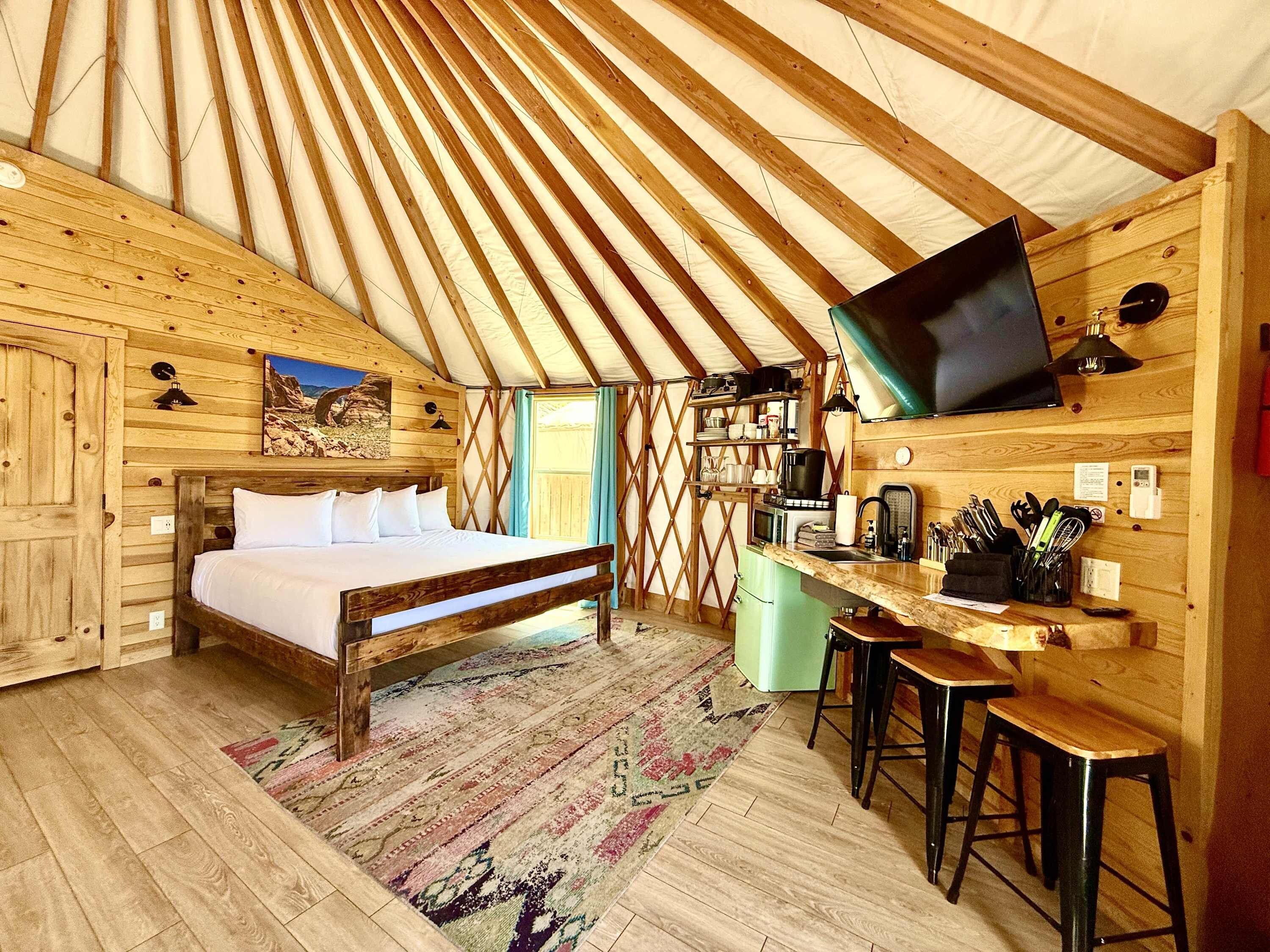 Un interior acogedor de madera con una cama, un pequeño rincón de cocina y un televisor en la pared.