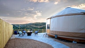 Une yourte avec vue sur les montagnes, une clôture en bois et un espace extérieur aménagé avec des chaises et une table.
