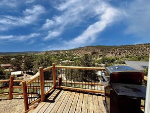 A wooden deck with a barbecue grill, overlooking a hilly landscape with scattered houses and greenery. - Glamping Yurt near Zion with 2 King Beds & Views (Orderville)