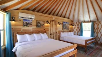 Una yurta con dos camas de madera, aire acondicionado de pared y una ventana con cortinas.