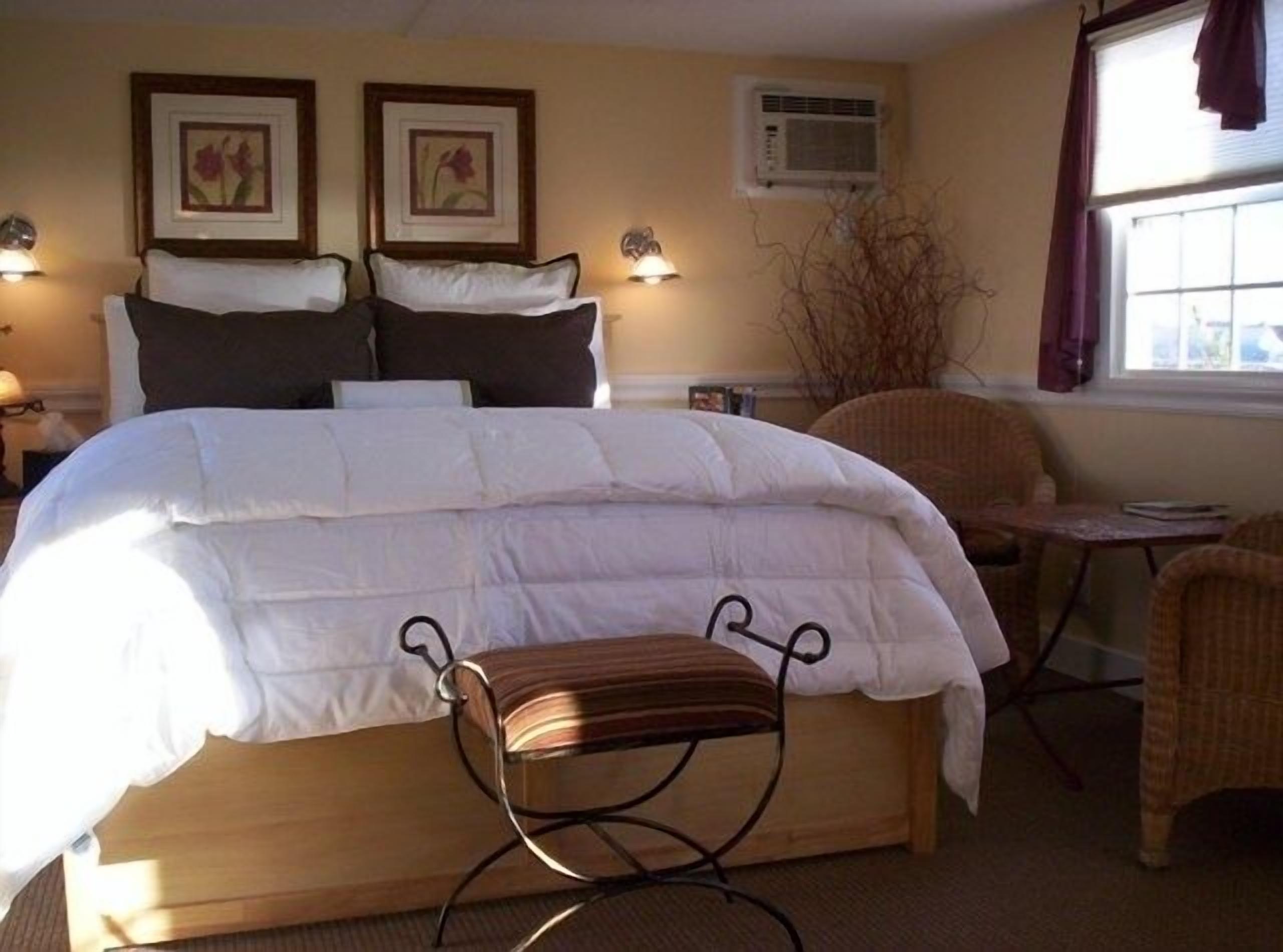 A hotel room with a large bed, two wall-mounted lamps, a window with curtains, and a small table with chairs.