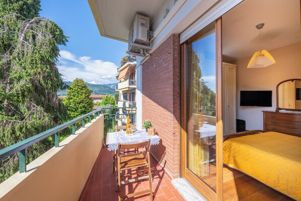 A balcony with a table and chairs, a bed with a yellow bedspread, and a TV in a bedroom.