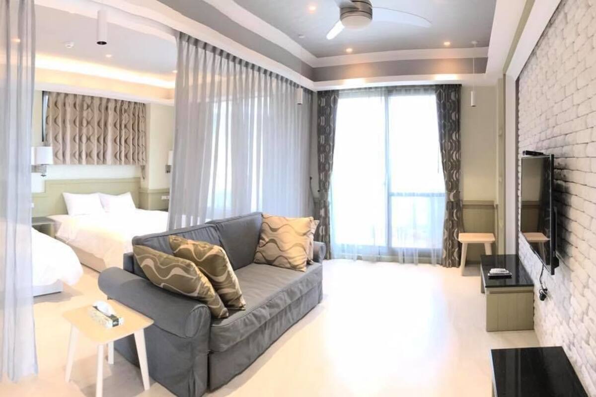 A modern hotel room with a bed, a sofa, a TV, and a minibar.