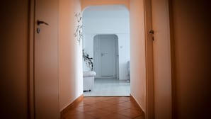 Un corridoio con una porta bianca in fondo, che conduce a una stanza con una porta e una sedia, entrambi bianchi.