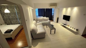 Un soggiorno moderno con divano, tavolino, televisore e una piccola mensola con oggetti decorativi.
