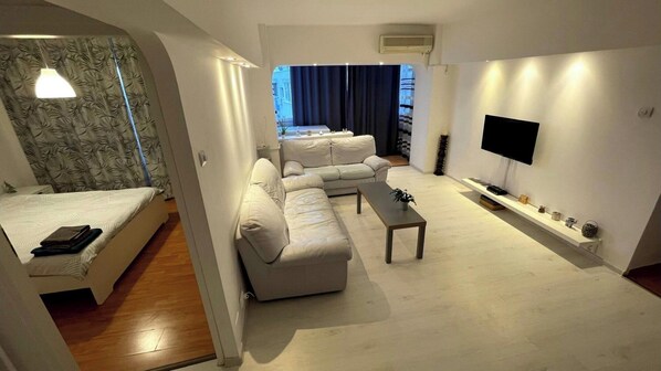 A modern living room with a sofa set, a coffee table, a TV, and a small shelf with decorative items.