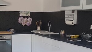 Een moderne keuken met witte kasten, een zwarte spatwand en een grijze betegelde vloer.