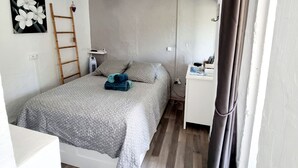 Een slaapkamer met een bed, nachtkastje, lamp, ladder, wandlamp en gordijn.