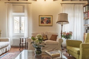 A living room with a sofa, a coffee table with a book and a vase, a lamp, and a painting on the wall.