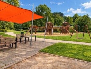 Une aire de jeux avec des structures en bois, un espace de repos abrité et un ciel dégagé.