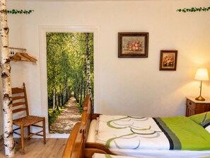 Une chambre à coucher avec un lit, une chaise, un tableau représentant un sentier de forêt et une lampe.