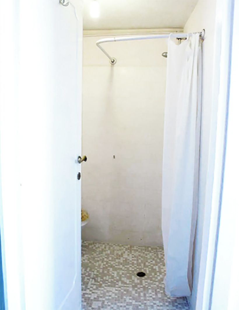 Un petit espace douche fermé, doté d’un sol carrelé et d’un rideau de douche.