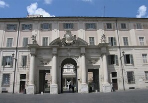 A large, historic building with a central archway, columns, and decorative elements.