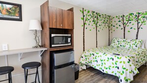 A compact room with a bed, a microwave, a refrigerator, a small bar area, and a green curtain. - Whitehall Cottages Boutique Motel - Full Beds (Whitehall)