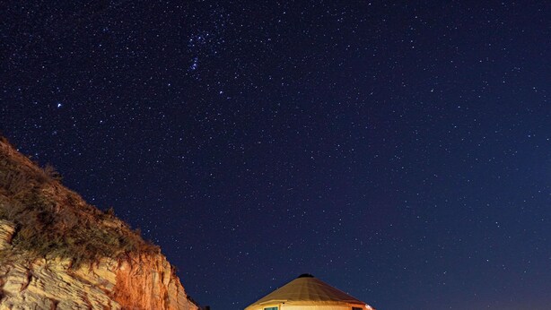 A yurt-style tent with a conical roof, situated on a gravel path beside a rocky cliff. - Glamping Yurt near Zion with Sunset Views (Orderville)