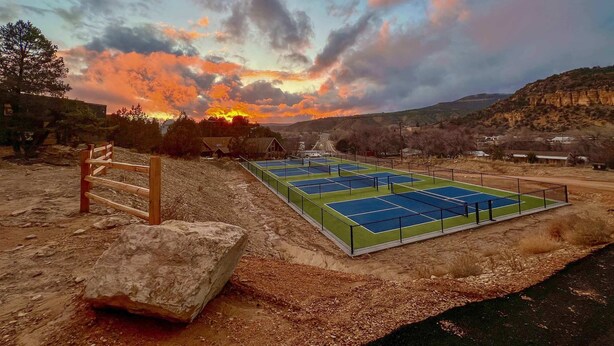 A tennis court with a wooden fence and a large rock nearby. - Glamping Yurt near Zion with Sunset Views (Orderville)