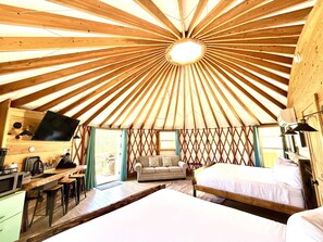 Interieur van een joert met een centrale koepel, een bank, een bed, een bureau met een computer en een keukenhoek.