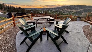 An outdoor seating area with a fire pit, surrounded by a wooden fence, overlooking a scenic valley. - Glamping Yurt near Zion with Sunset Views (Orderville)