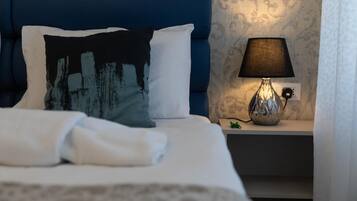 A neatly made bed with white linens, a blue headboard, and a decorative pillow. There is a bedside lamp on a nightstand beside the bed.